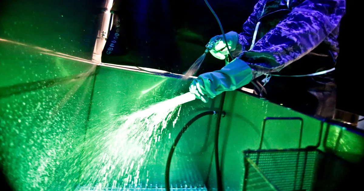Technician spraying a metal part with fluorescent penetrant under ultraviolet light, the dye penetrant method used for crack detection