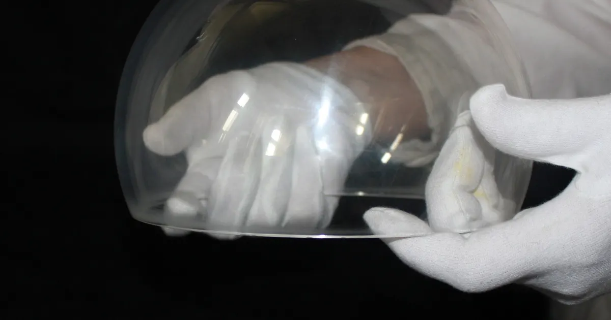 Clear sapphire hemisphere dome held in white gloves, a single crystal aluminium oxide part